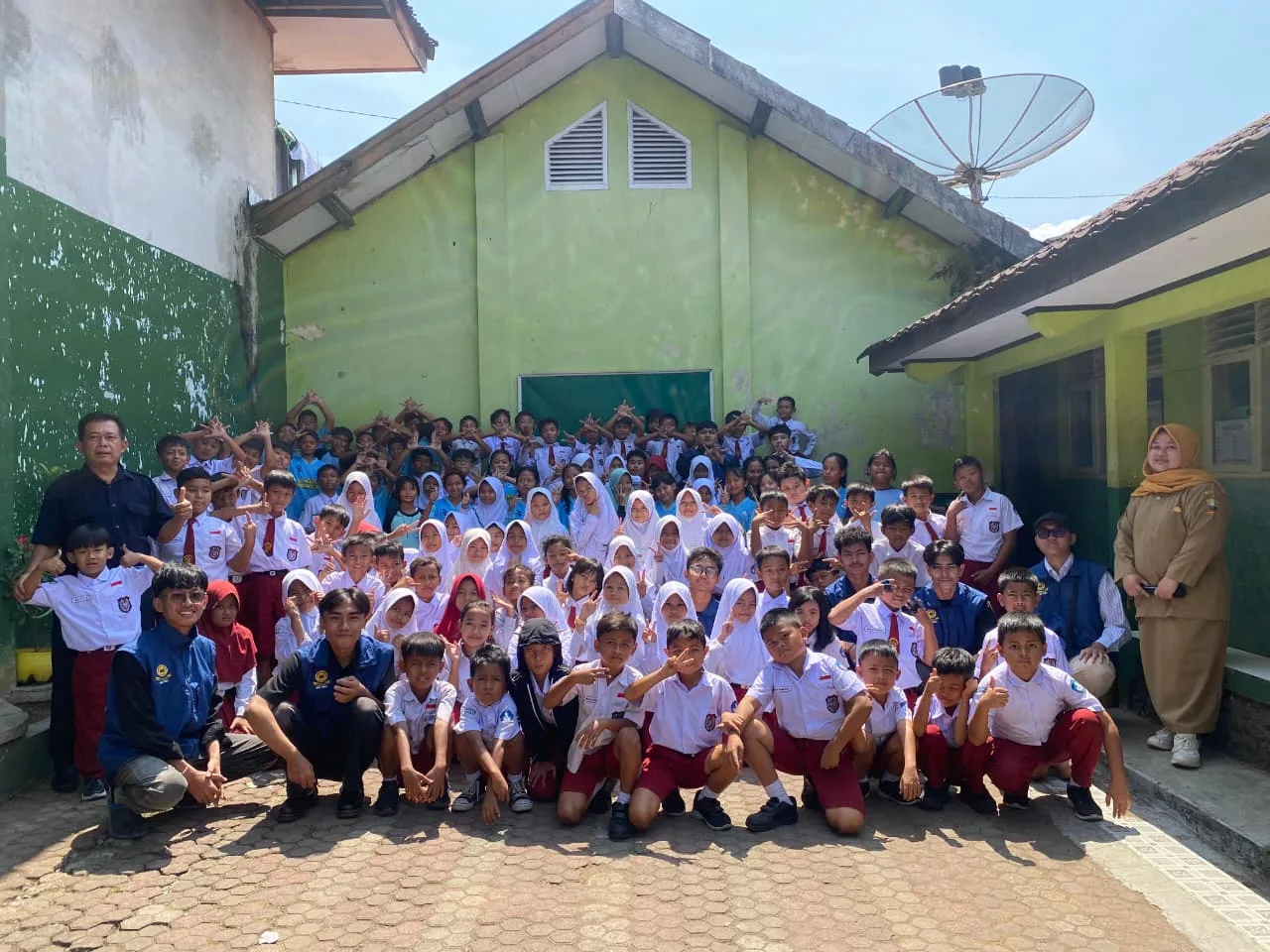 Foto bersama seluruh siswa, dewan guru, dan mahasiswa di halaman sekolah SDN Darmaraja II setelah kegiatan pembelajaran informatika.